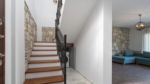 Uma escadaria com degraus de madeira e parede de pedra, que leva a uma sala de estar com sofá azul e parede de pedra.