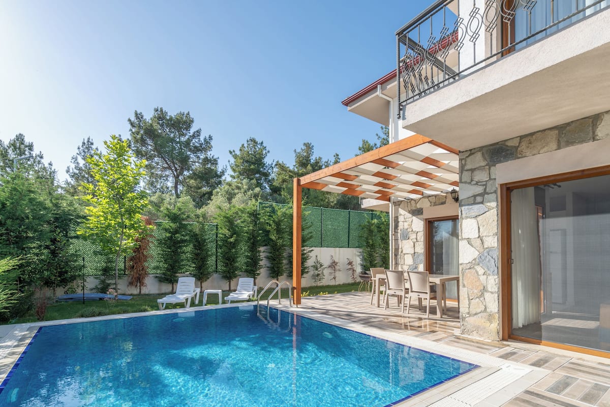 Une piscine avec des chaises longues, une pergola et un mur en pierre.