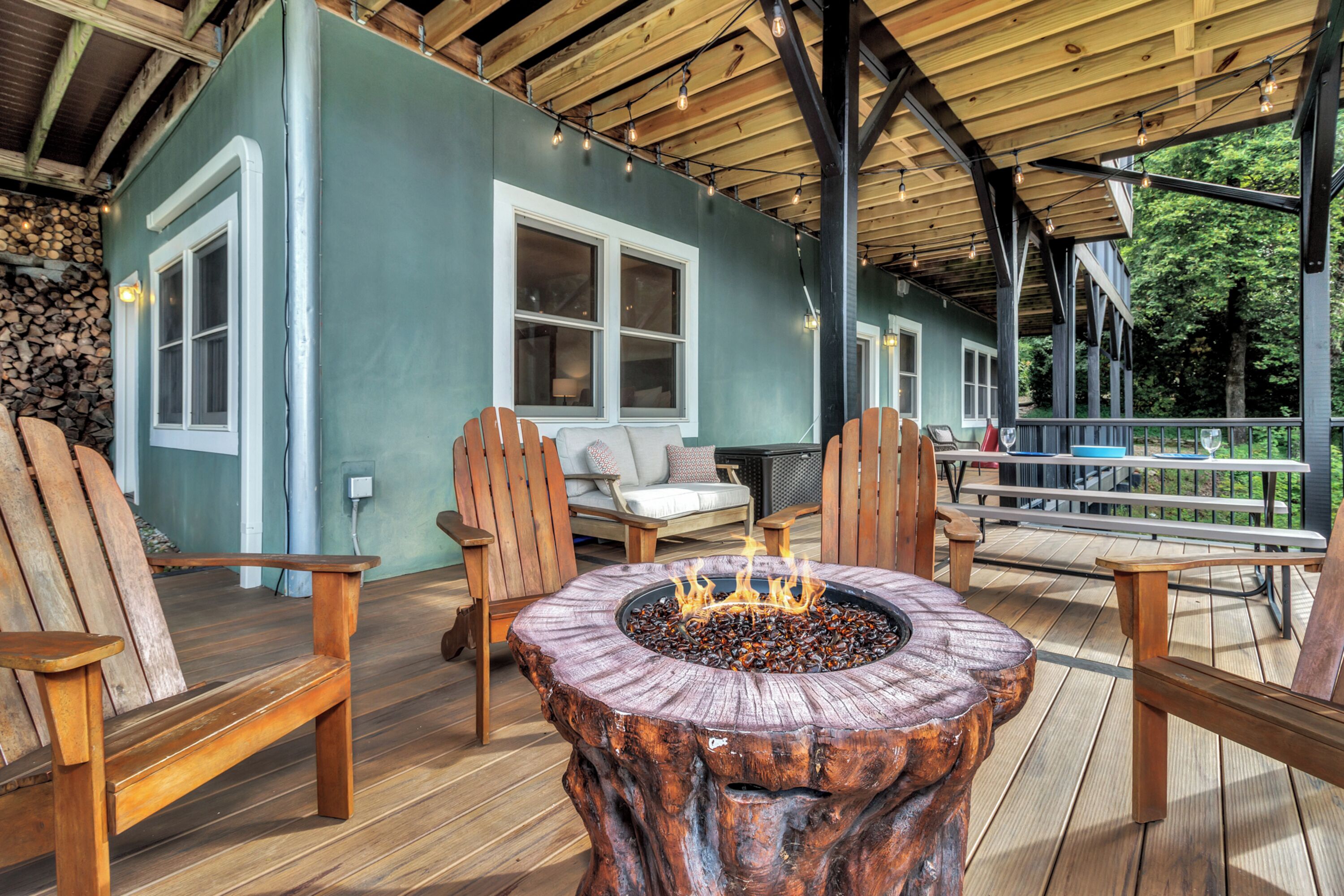 A wooden deck with a fire pit, outdoor seating, and a covered area with a view of the surrounding trees.