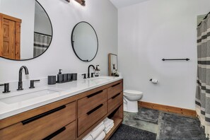 Un bagno moderno con un mobile bagno in legno, due lavabi, un water e una tenda da doccia.