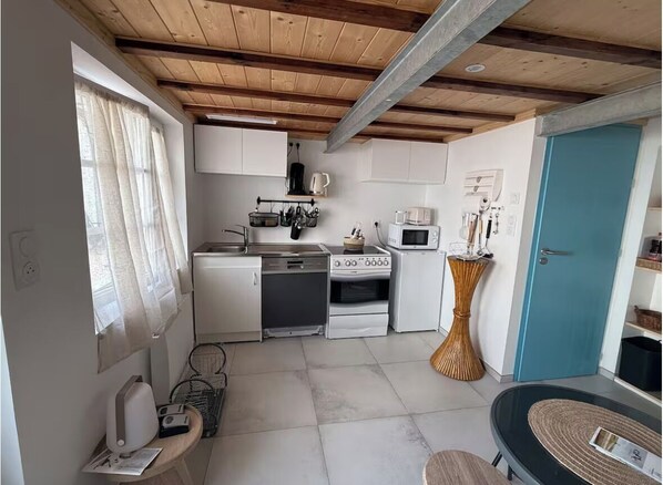 A compact kitchen with white cabinets, a microwave, stove, and a sink. There is a window with curtains, a door, and a small table with a basket.