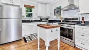 A modern kitchen with white cabinetry, stainless steel appliances, and a wooden island. - Quaint Mill Cottage (Marion)
