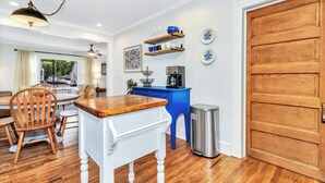 A dining area with a wooden table and chairs, a blue cabinet with shelves, and a trash can. - Quaint Mill Cottage (Marion)
