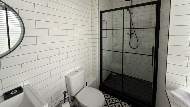 A bathroom with white subway tiles, a toilet, a glass-enclosed shower, and a round mirror.
