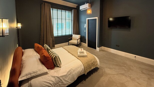 Un dormitorio moderno con una cama grande, una ventana con cortinas, una lámpara en el techo y un televisor de pantalla plana montado en la pared.