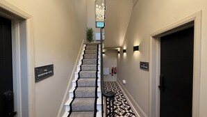 Una escalera con piso de diseño geométrico, una lámpara moderna y dos puertas identificadas como "The Mackintosh Room" y "The Pitch Hall Room".
