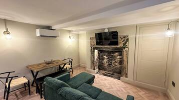 A cozy living room with a fireplace, a dining area with a wooden table and chairs, and a green sofa.