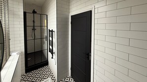 Un baño con azulejos blancos tipo metro, una puerta negra y una zona de ducha con puerta de cristal.