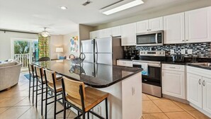 Una cocina moderna con armarios blancos, una isla central con taburetes de bar, refrigerador, microondas, horno y un backsplash de azulejos.
