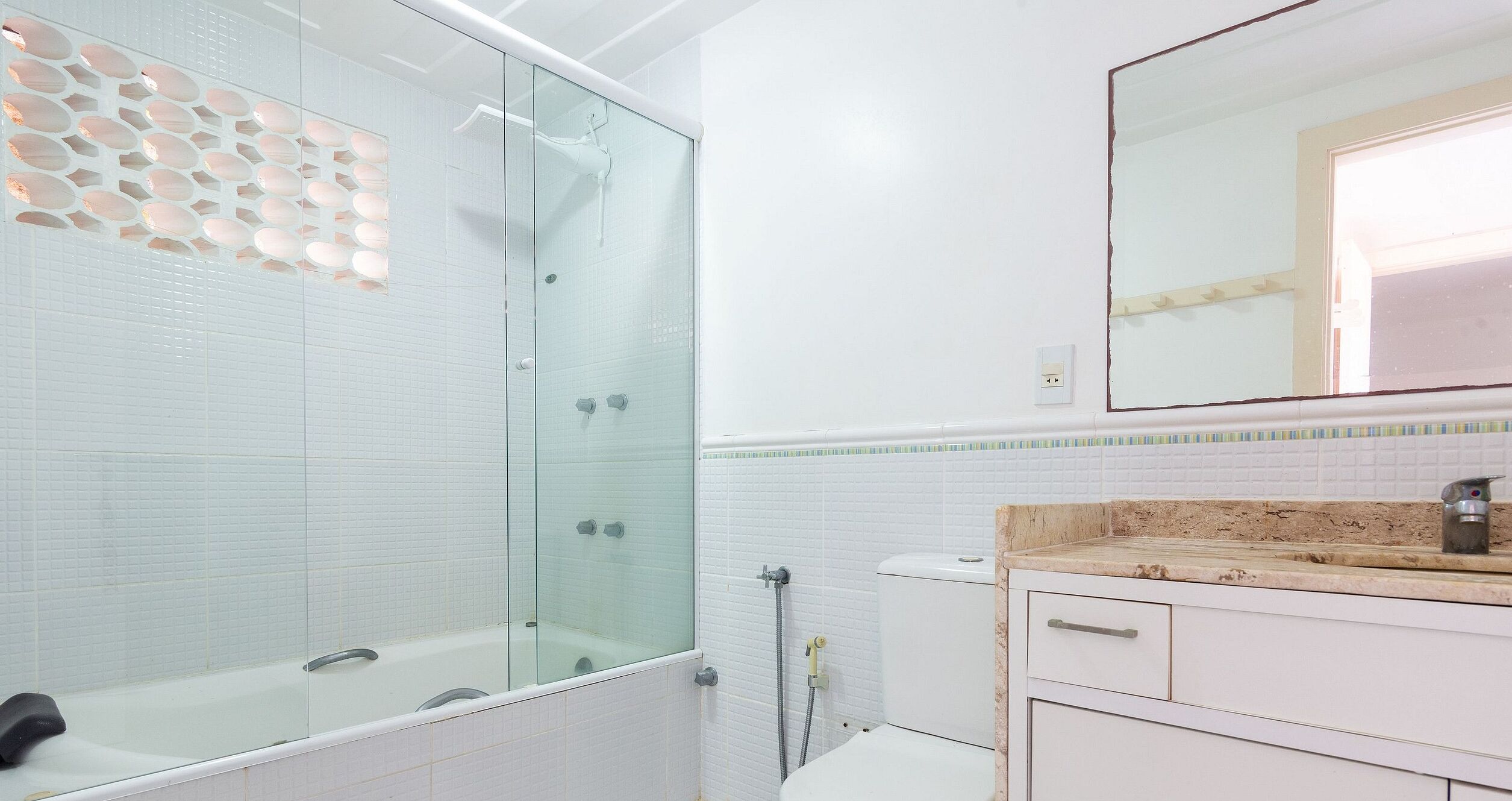 Un baño con ducha de vidrio, inodoro blanco y lavamanos con encimera color beige.