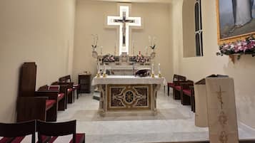 A church interior with pews, a central altar, a cross, and a painting.