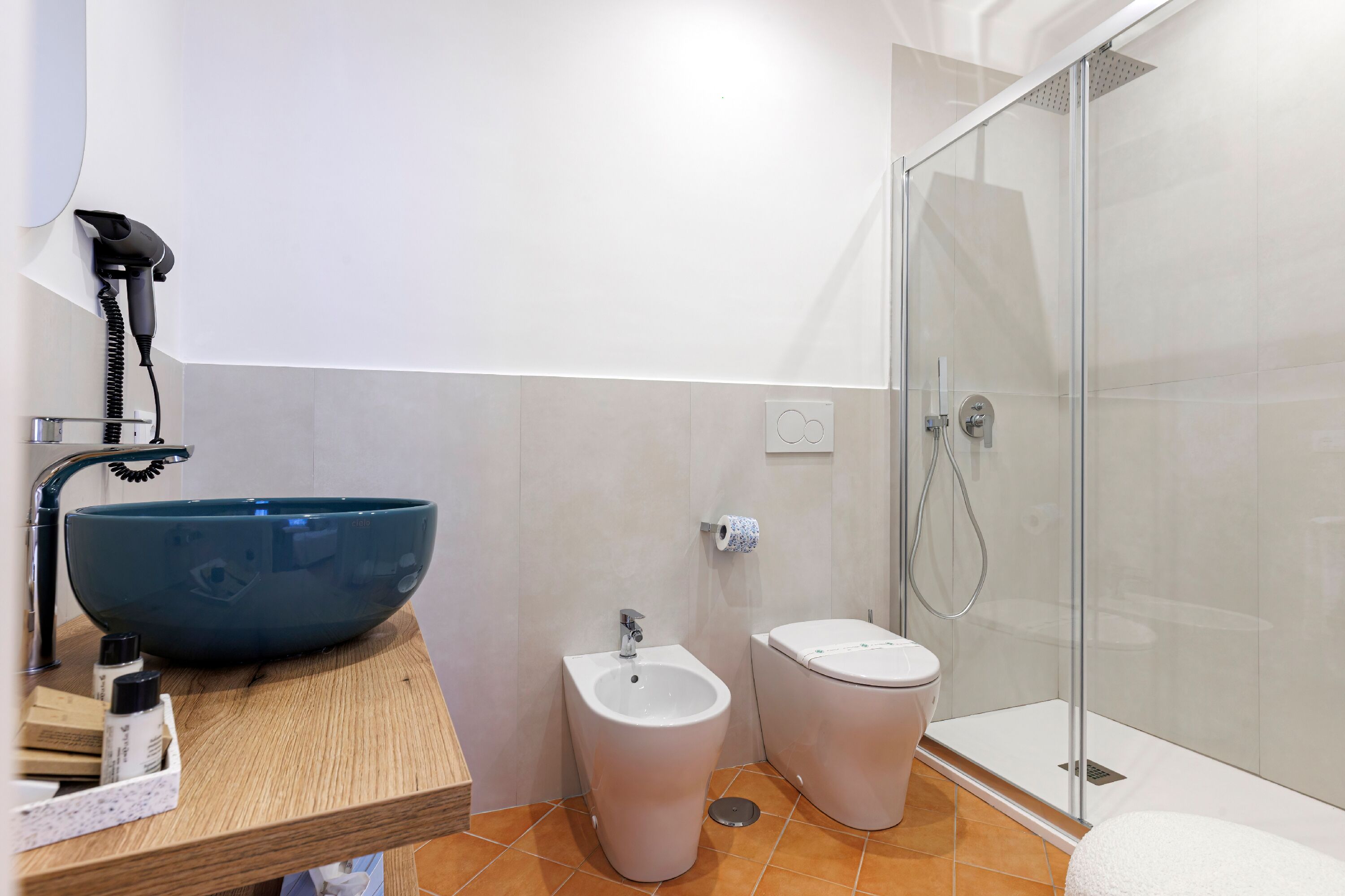 Une salle de bain dotée d’un grand lavabo bleu, d’un bidet et d’une douche à parois de verre.