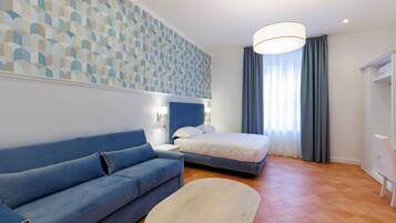 Una habitación de hotel moderna con un sofá azul, una cama con ropa de cama blanca, una mesa de centro de madera y una pared con un diseño estampado.