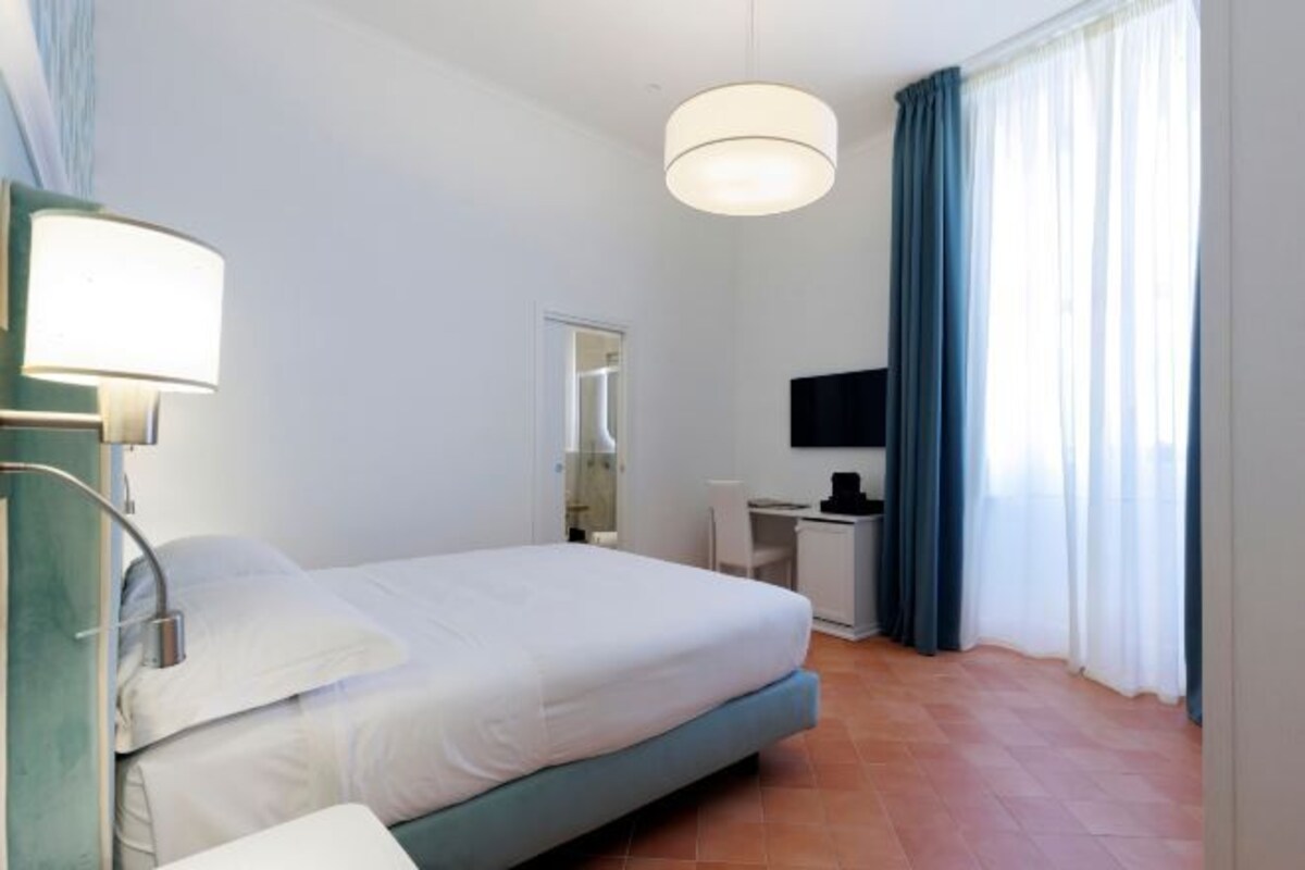 A hotel room with a bed, a desk, a chair, a TV, and a window with curtains.