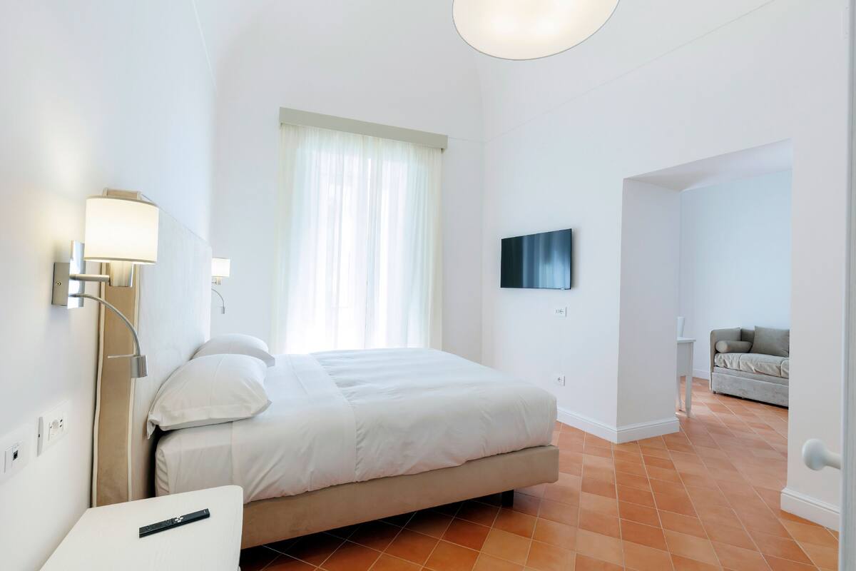 Una habitación de hotel moderna con una cama grande, un televisor en la pared y una mesita de noche con una lámpara.