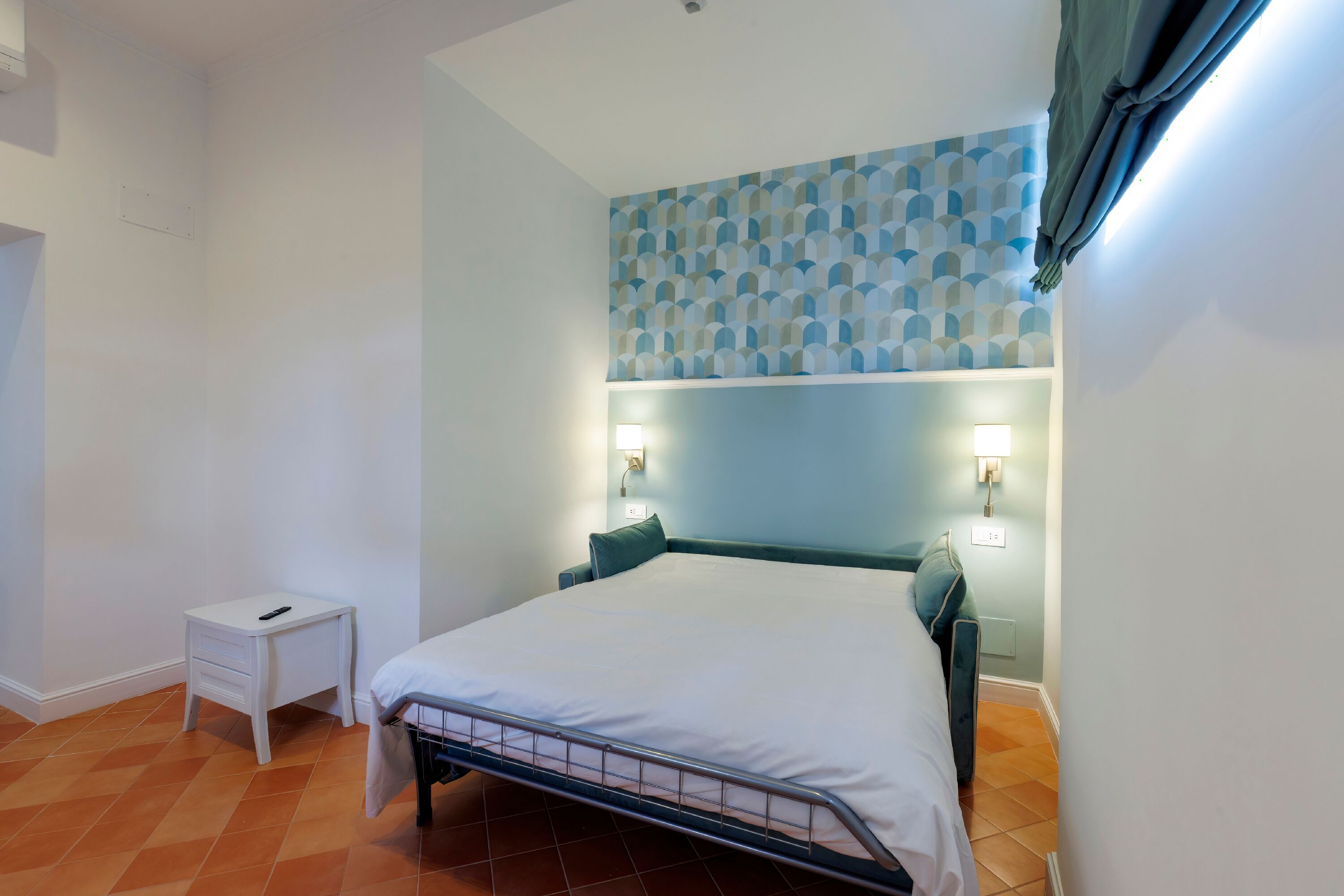 A bedroom with a bed, bedside lamps, a nightstand, and a patterned wall.