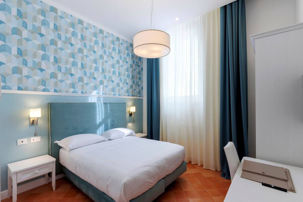 Una habitación de hotel con una cama, mesitas de noche, un escritorio y una lámpara.