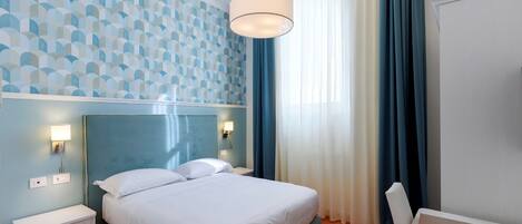 Una habitación de hotel con cama, mesitas de noche, un escritorio y una lámpara.