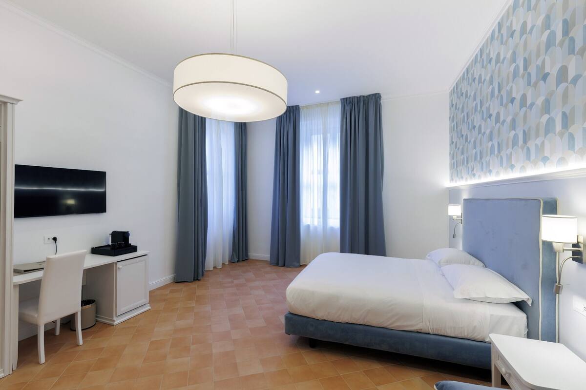 Habitación de hotel con cama, escritorio, silla, televisor y pared con estampado.