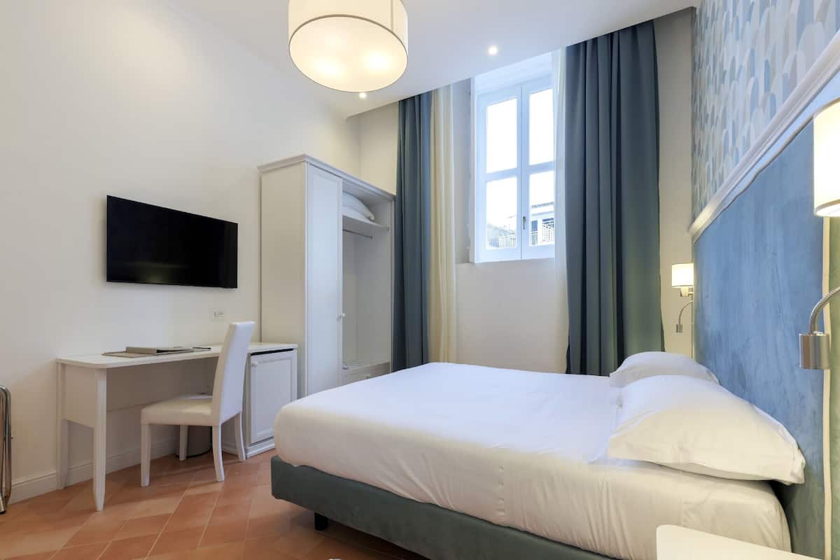 Una habitación de hotel con cama, escritorio, silla, televisión y armario.