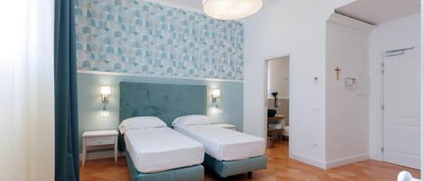 A hotel room with two beds, a blue headboard, a patterned wall, and a large window with curtains.