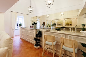 Una cocina moderna con armarios blancos, una isla central con taburetes de bar y plantas decorativas.