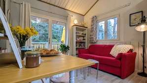 Ett mysigt vardagsrum med en röd soffa, ett matbord i trä och en bokhylla.