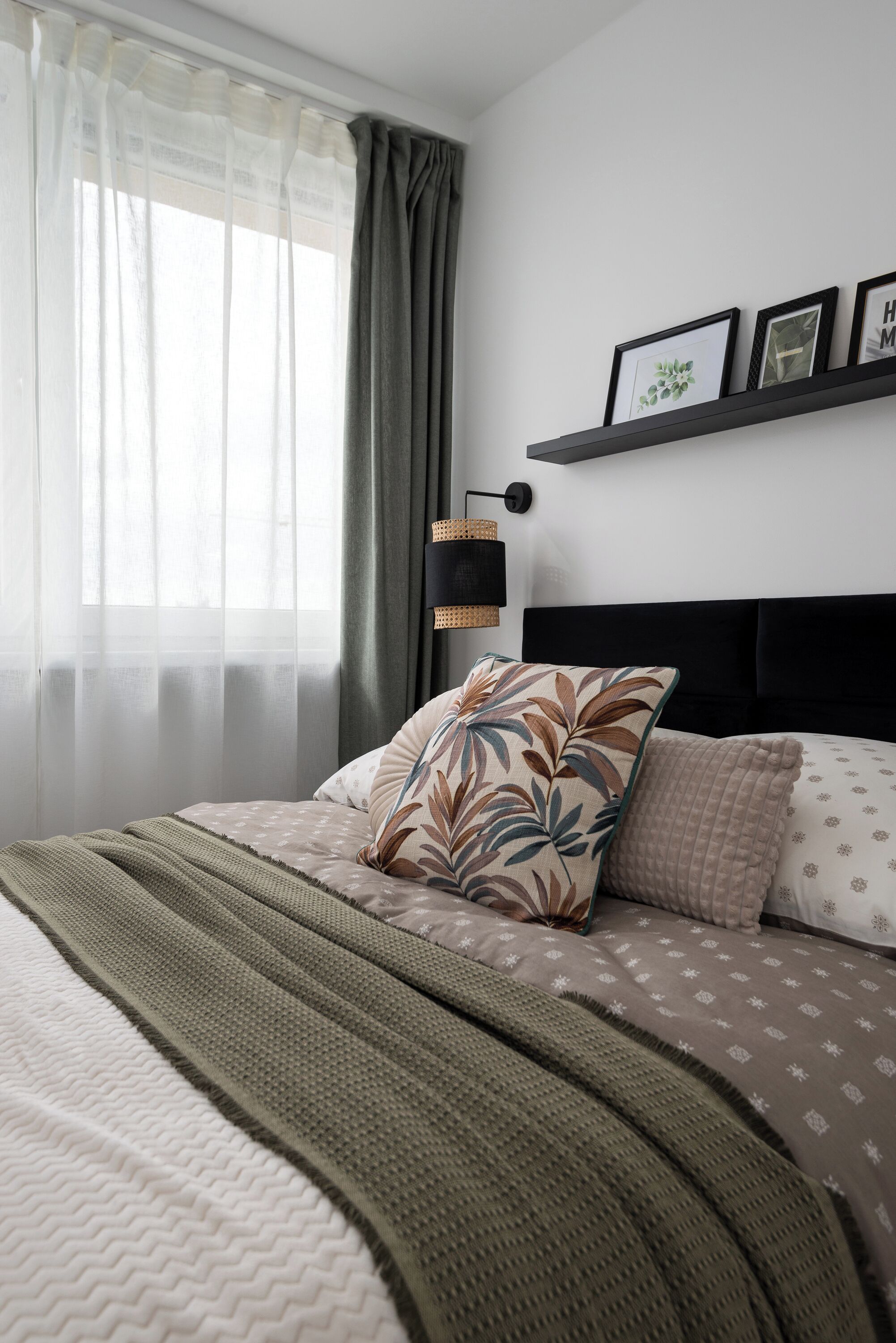 A neatly made bed with a patterned pillow and a green blanket, a bedside lamp, and a shelf with framed pictures.