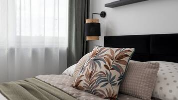 A neatly made bed with a patterned pillow and a green blanket, a bedside lamp, and a shelf with framed pictures.