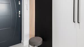 A modern interior with a dark door, a white wall with a black panel, a wooden slat wall, a grey bench, and a coat rack. - Amber - by Kairos Apartments (Gliwice)