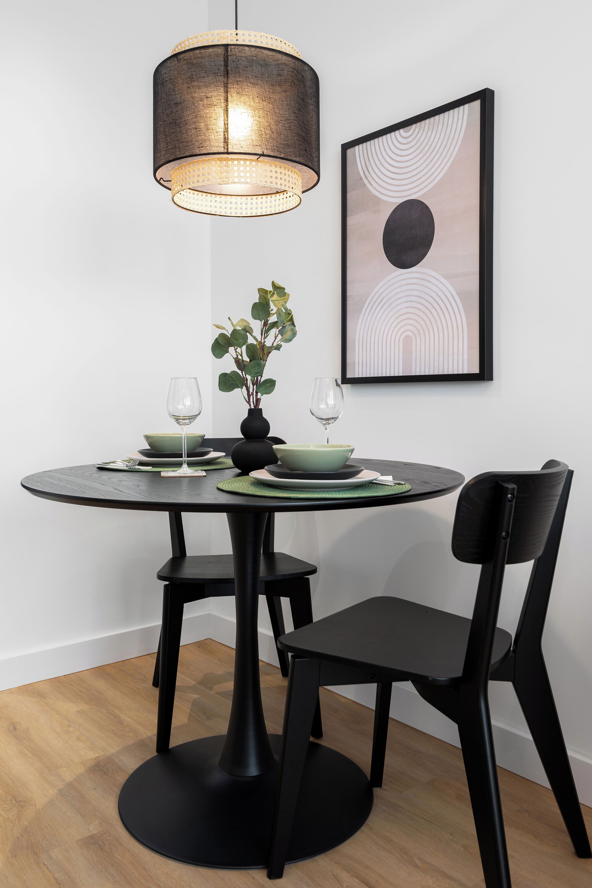 A dining table with a black chair, a pendant light, and a framed abstract painting on the wall.