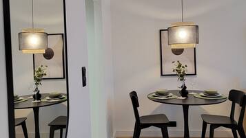 A dining area with a round table, black chairs, and two pendant lights. A large mirror is mounted on the wall to the left.