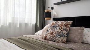 A neatly made bed with a patterned pillow, a bedside lamp, and a shelf with framed pictures. - Amber - by Kairos Apartments (Gliwice)
