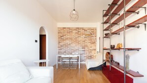 Una sala de estar moderna con un sofá blanco, una mesa de comedor con sillas, una pared de ladrillo y un mueble de estanterías rojo.
