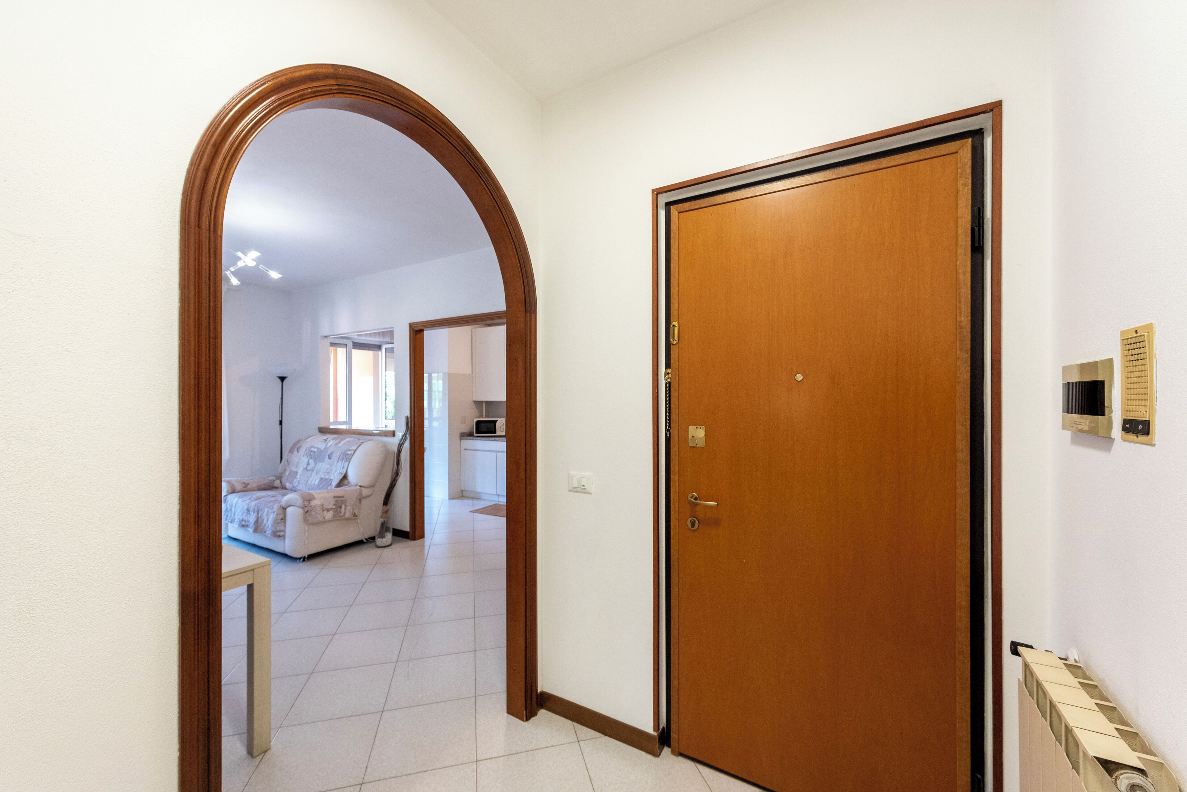 A hallway with a wooden door, a tiled floor, and a white wall.
