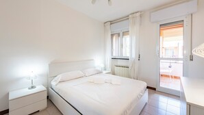 Un dormitorio con cama, mesita de noche, escritorio y ventana con cortinas.