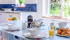 Una mesa de desayuno preparada con platos, tazones, tetera, cafetera, vasos de jugo de naranja y croissants.