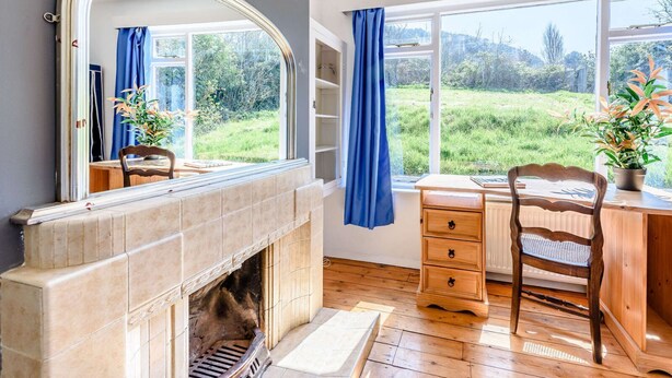 Una habitación con chimenea, un escritorio, una silla y un ventanal con vistas a zonas verdes.