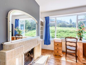 Una habitación con chimenea, un escritorio, una silla y un ventanal con vistas a zonas verdes.