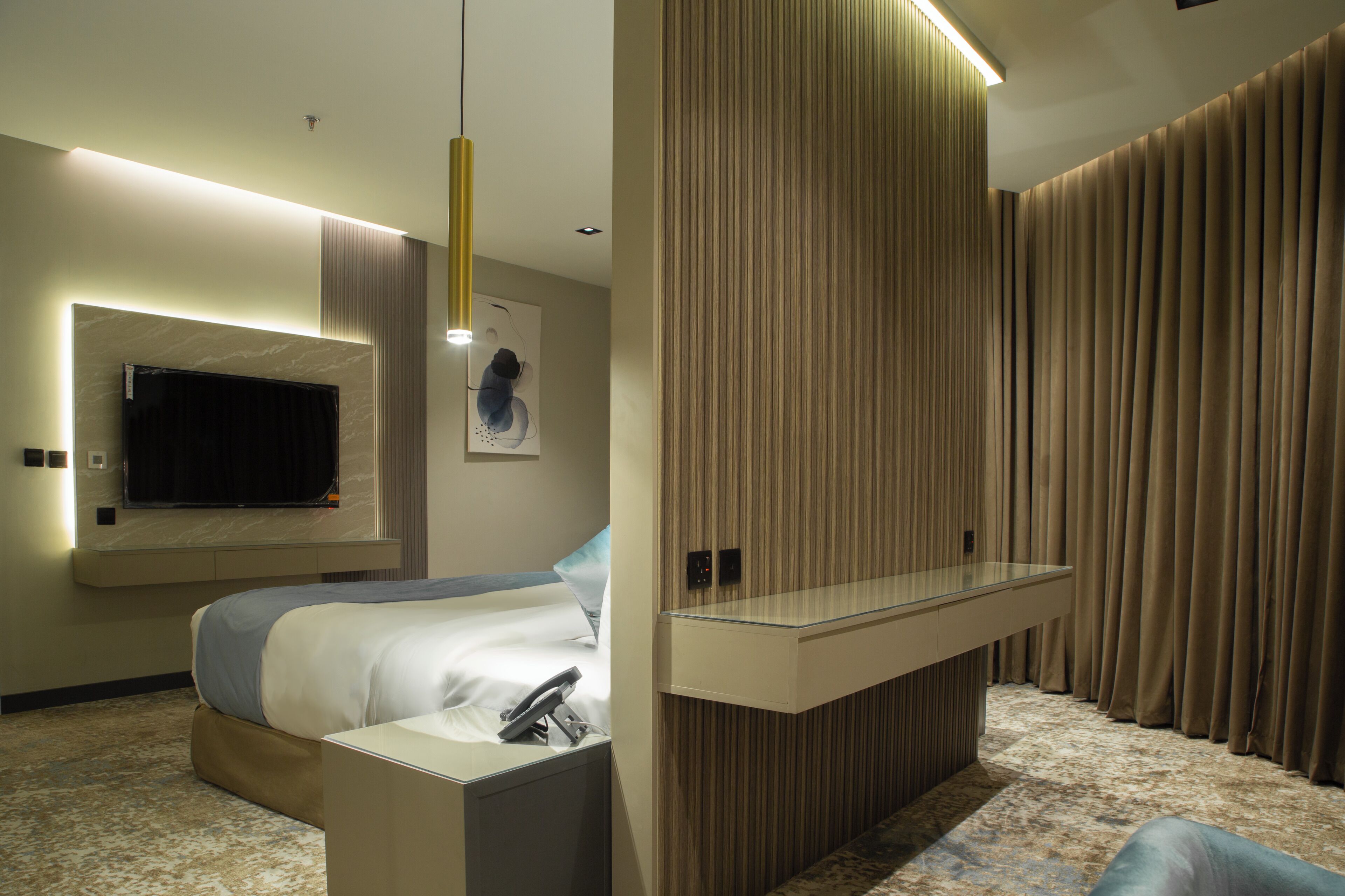 Ein modernes Hotelzimmer mit einem Bett, einem flachbildfernseher an der Wand, einer Glastrennwand und einem großen Fenster mit Vorhängen.