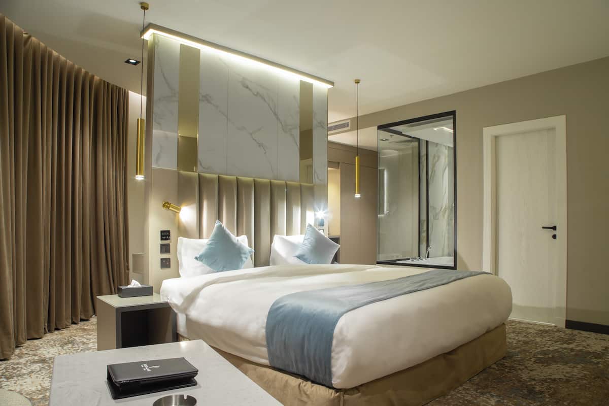 A modern hotel room with a large bed, a bedside table, a nightstand, a desk, and a large mirror.
