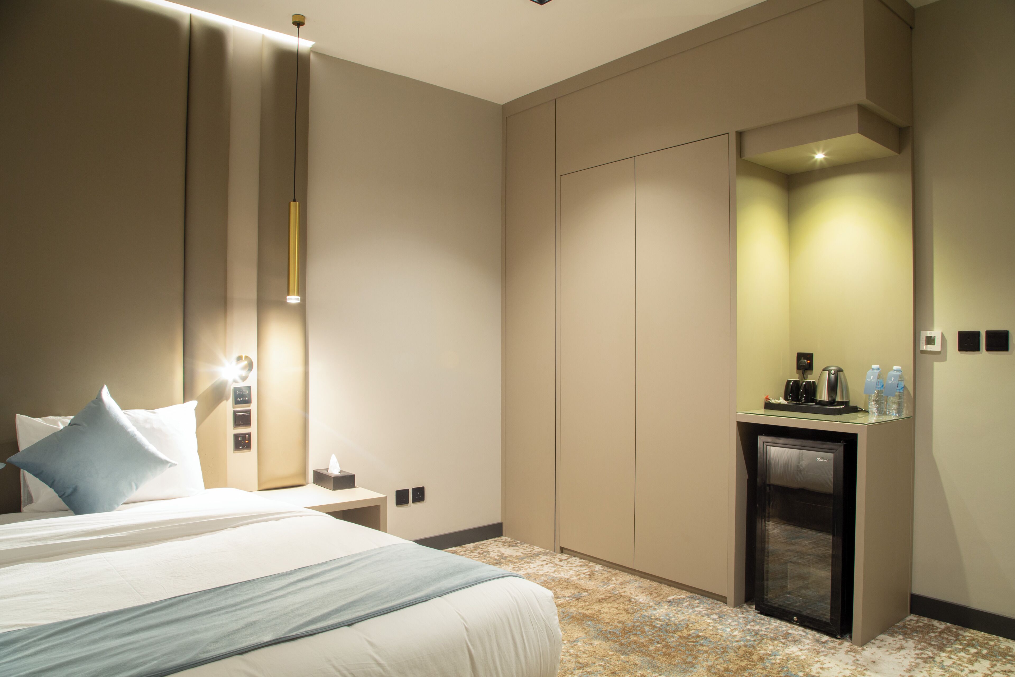 A hotel room with a bed, bedside table, nightstand, and a minibar.