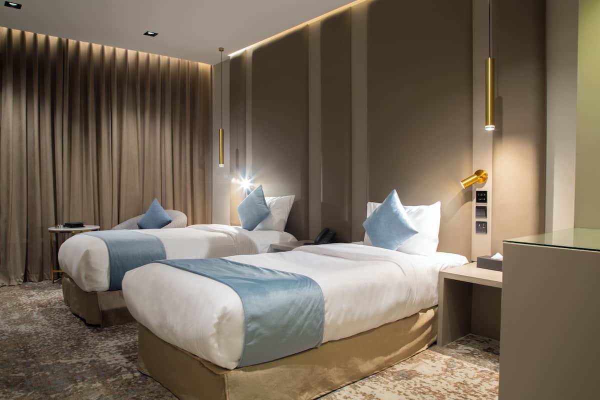 A hotel room with two beds, a desk, a nightstand, and a large window with curtains.