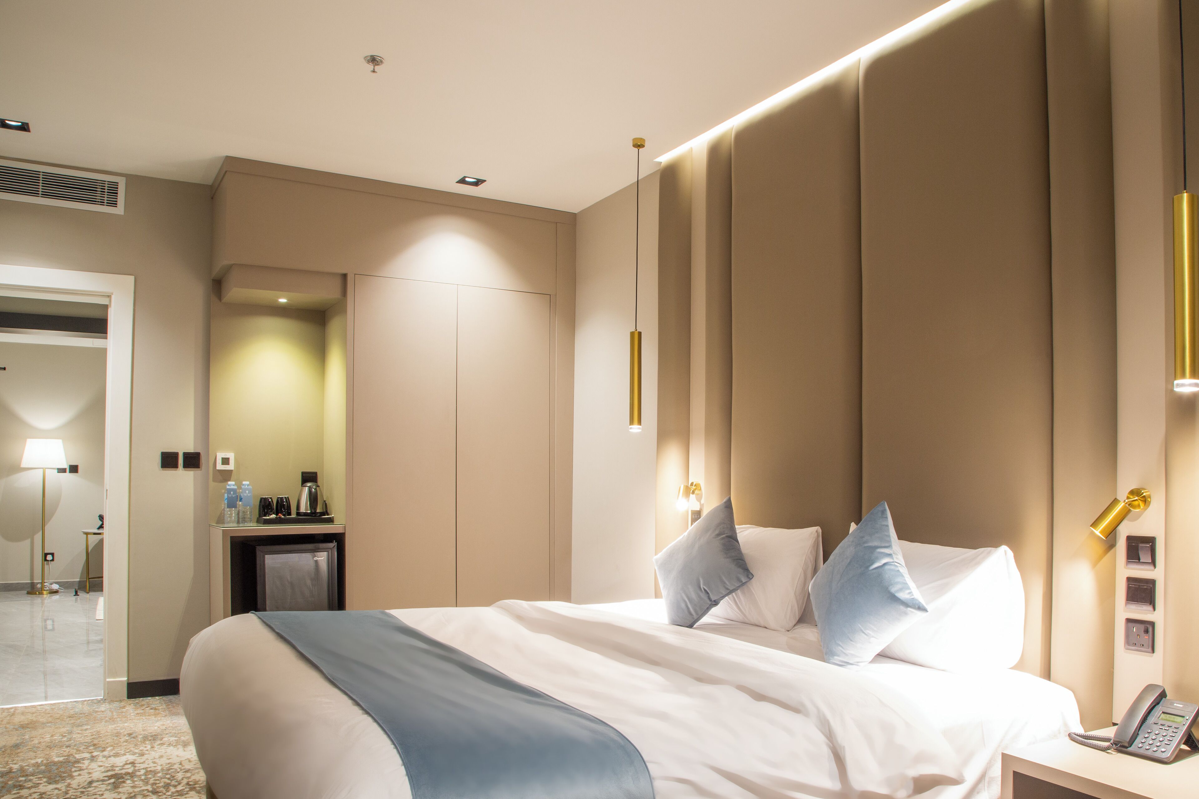 Habitación de hotel con una cama grande, mesita de noche con teléfono, y escritorio con lámpara y cafetera.