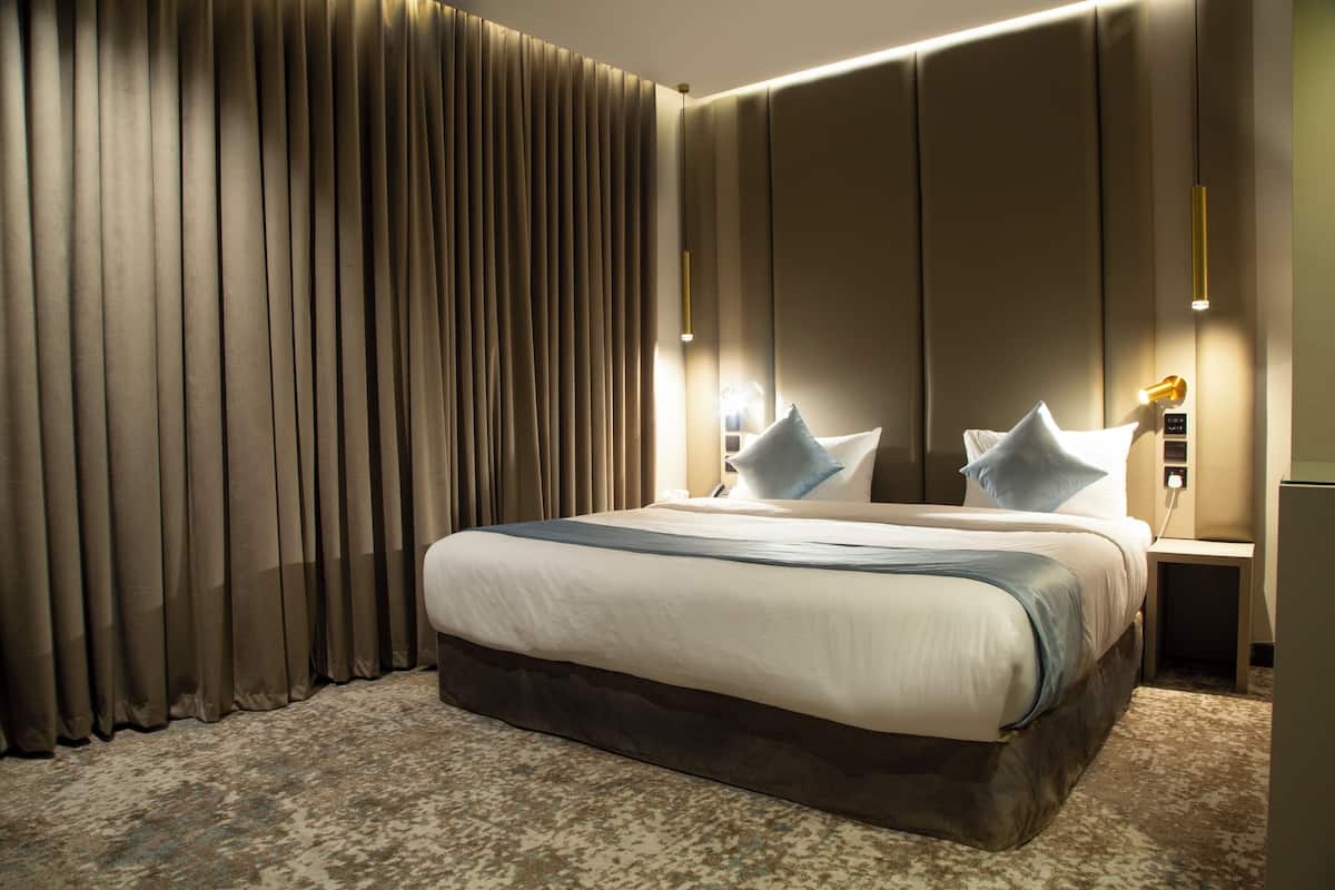 A hotel room with a large bed, a headboard, a nightstand, and a lamp.