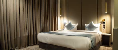 A hotel room with a large bed, a headboard, a nightstand, and a lamp.