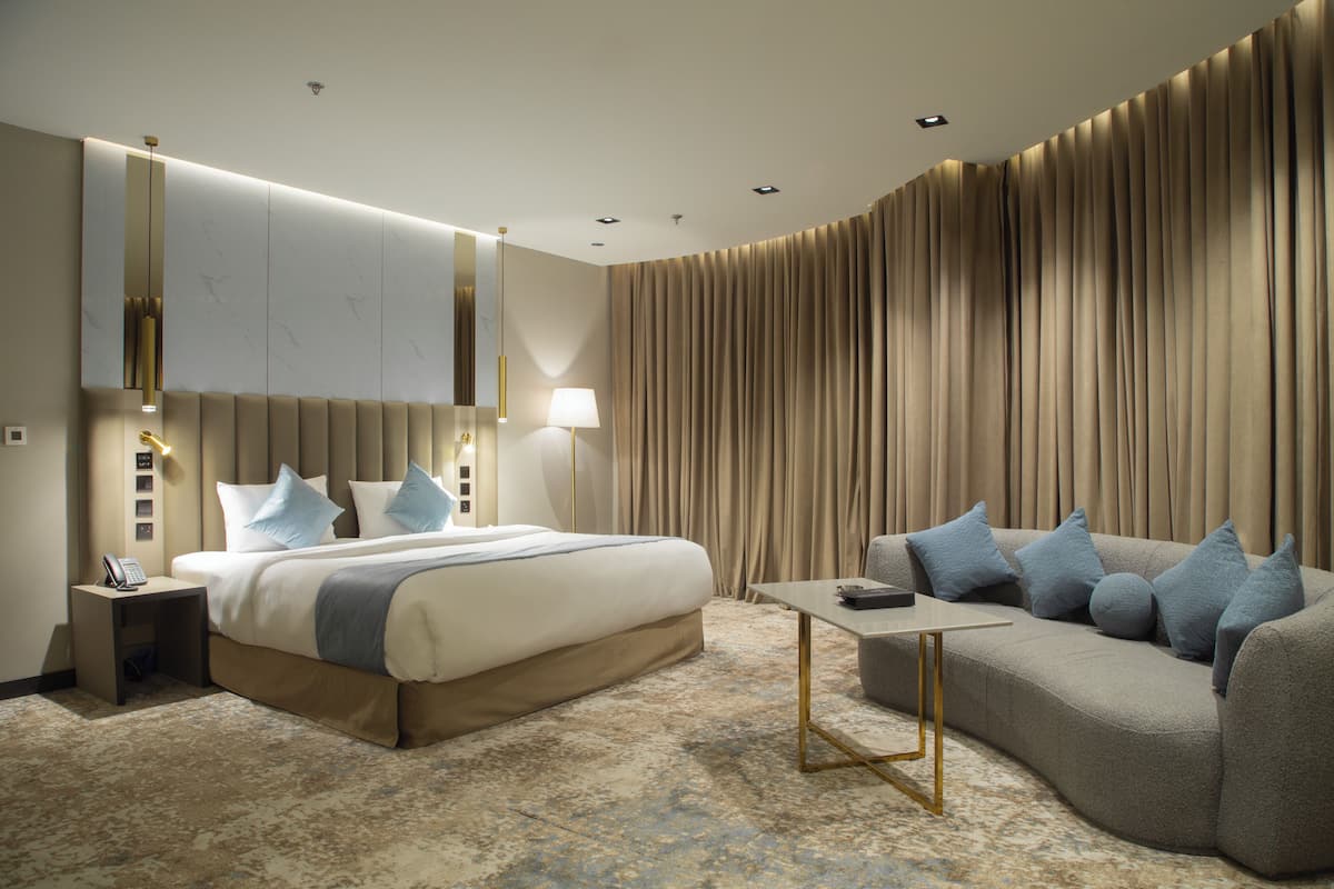 A modern hotel room with a large bed, a sofa, a small table, and a wall-mounted TV.