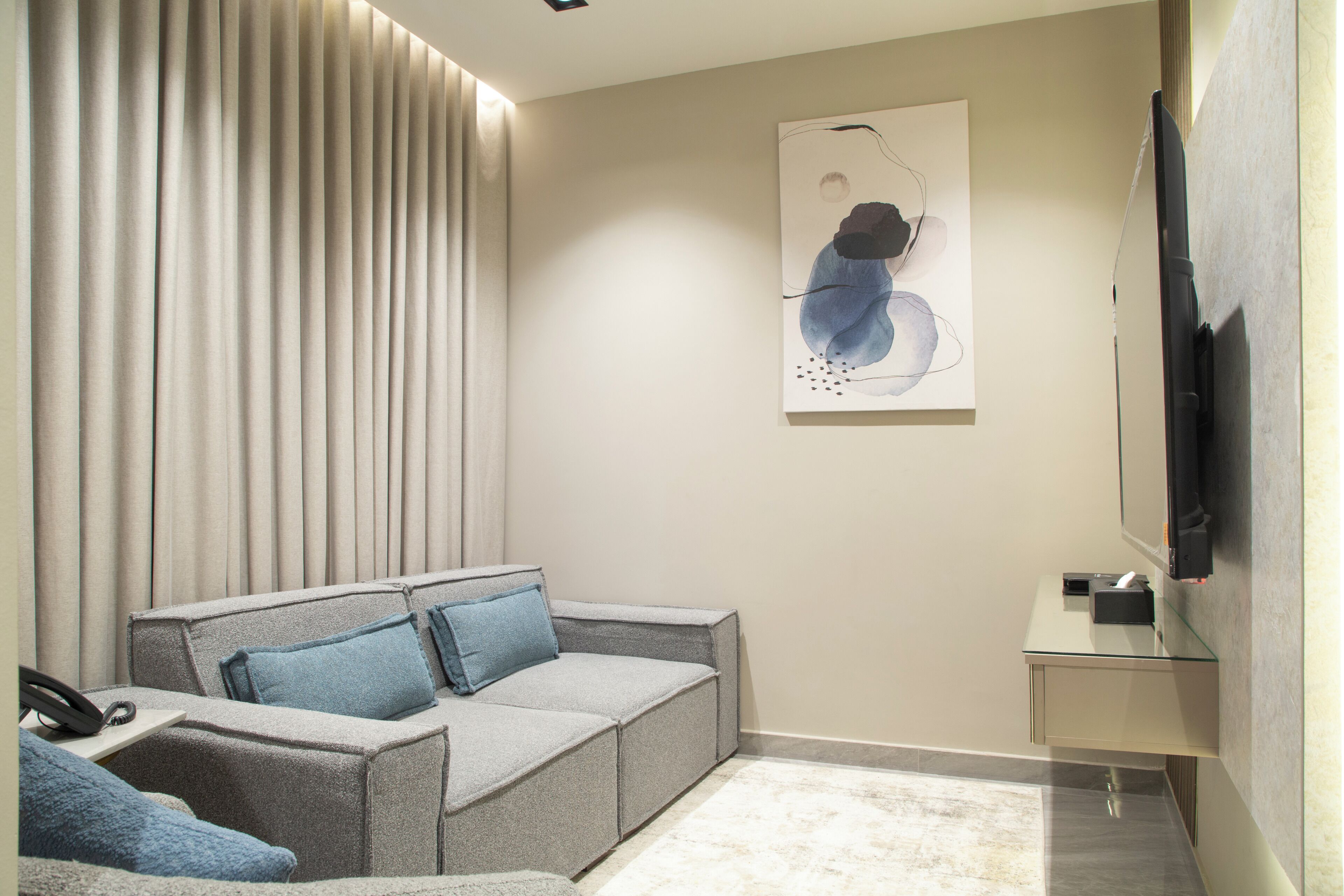 A modern living room with a grey sectional sofa, a flat-screen TV mounted on the wall, and a minimalist artwork above the sofa.