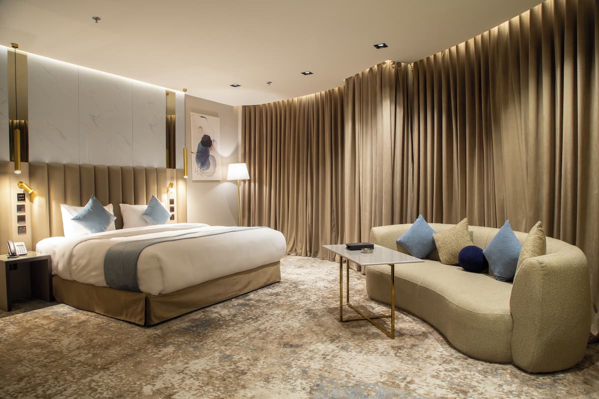 A hotel room with a bed, a sofa, a small table, and a large window with curtains.