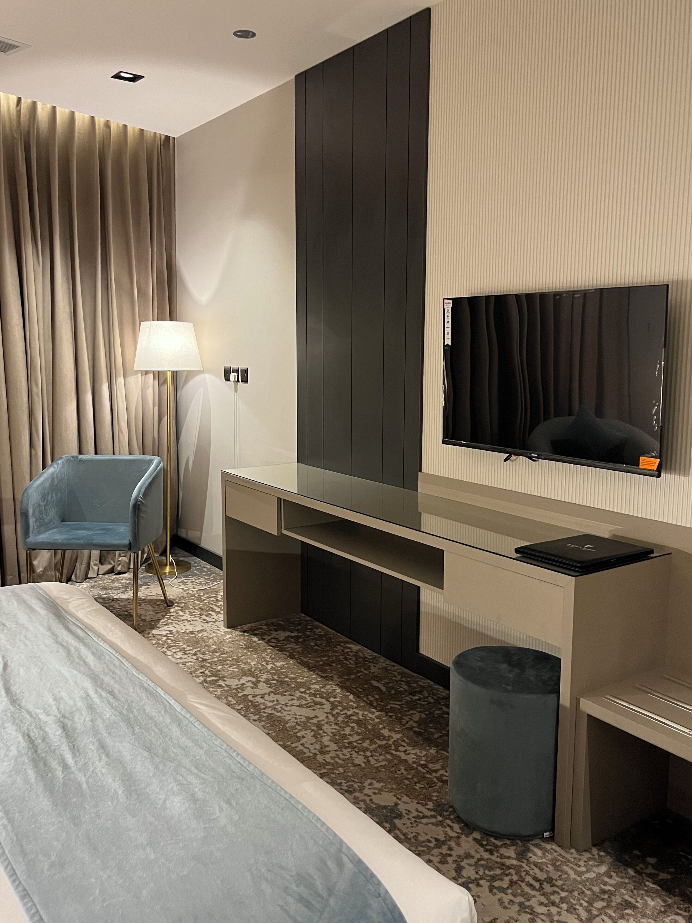 Habitación de hotel con cama, escritorio con televisor de pantalla plana, silla, lámpara y cesto de basura.